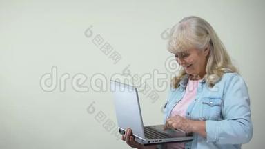 老年女士在笔记本电脑上打字，显示拇指向上，退休人员的电脑素养